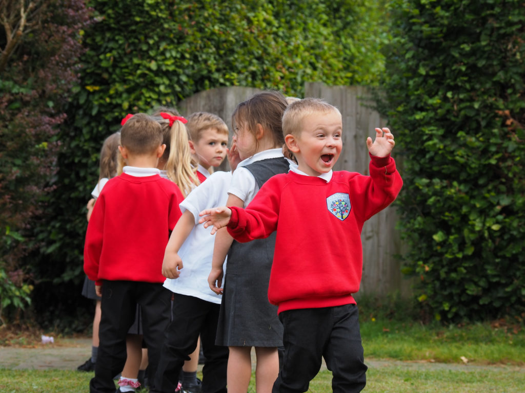 A small group of pupils are seen lining up together on the school grounds. A boy at the end of the line is seen smiling for the camera.