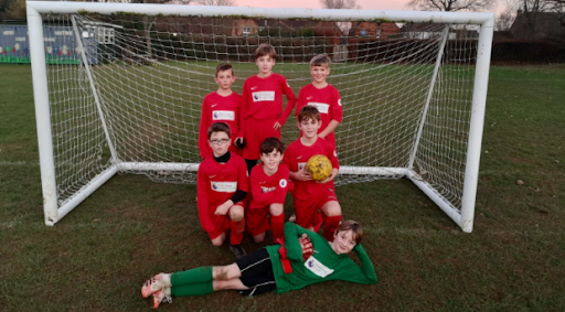A group of seven boys are seen posing for a photo together in a Football goal, after having played a match against Oaks Primary Academy.